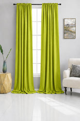 Beige curtains hanging in a living room with a couch and side table.
