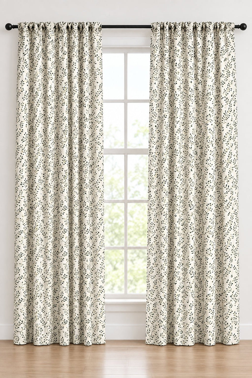 A pair of floor-length curtain panels with a black and white floral pattern, hanging on a black rod with matching grommets in front of a tall window.