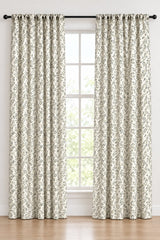 A pair of floor-length curtain panels with a black and white floral pattern, hanging on a black rod with matching grommets in front of a tall window.