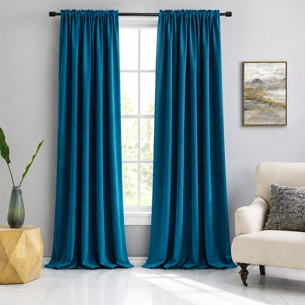 A pair of light blue curtain panels hanging on a black rod over a window in a bright room, with a cream armchair, framed wall art, and a small side table visible.